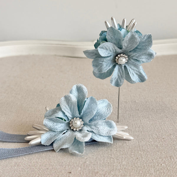 Pair of light blue floral hair accessories with ribbons on a beige surface.