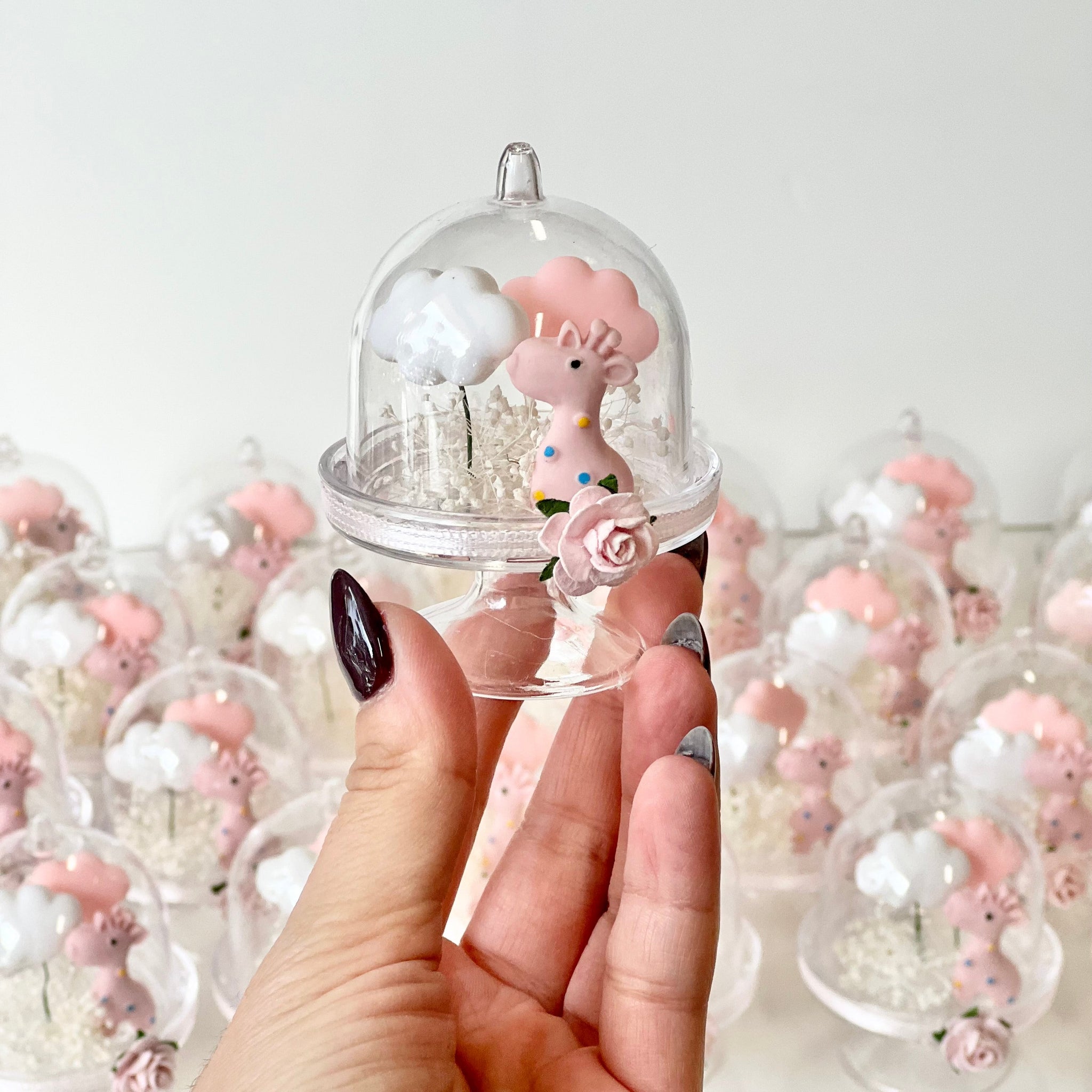 Small pink deer figurine under a glass dome held by a hand against a light background.