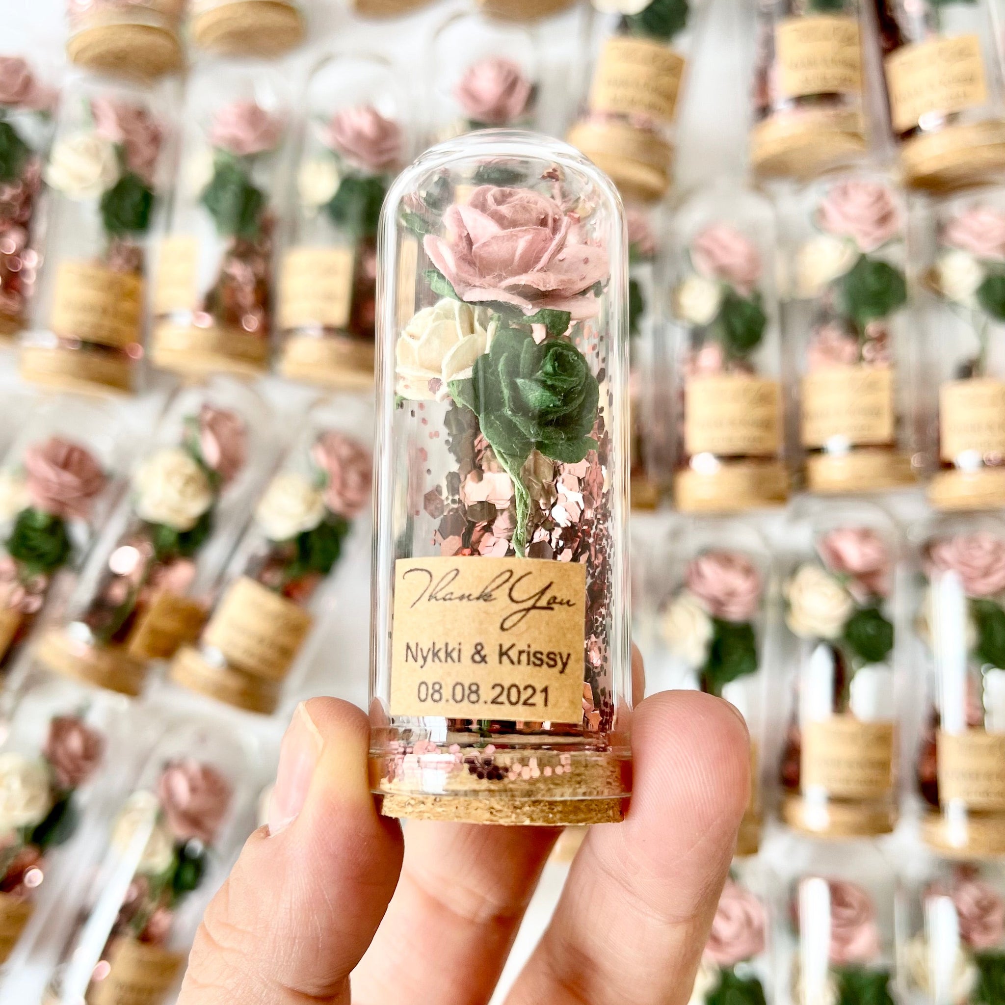 Clear tube with preserved flowers held by a hand, with a blurred background of similar tubes.