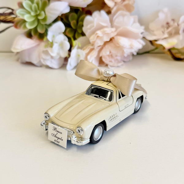 Model car with open doors on a white surface with flowers in the background