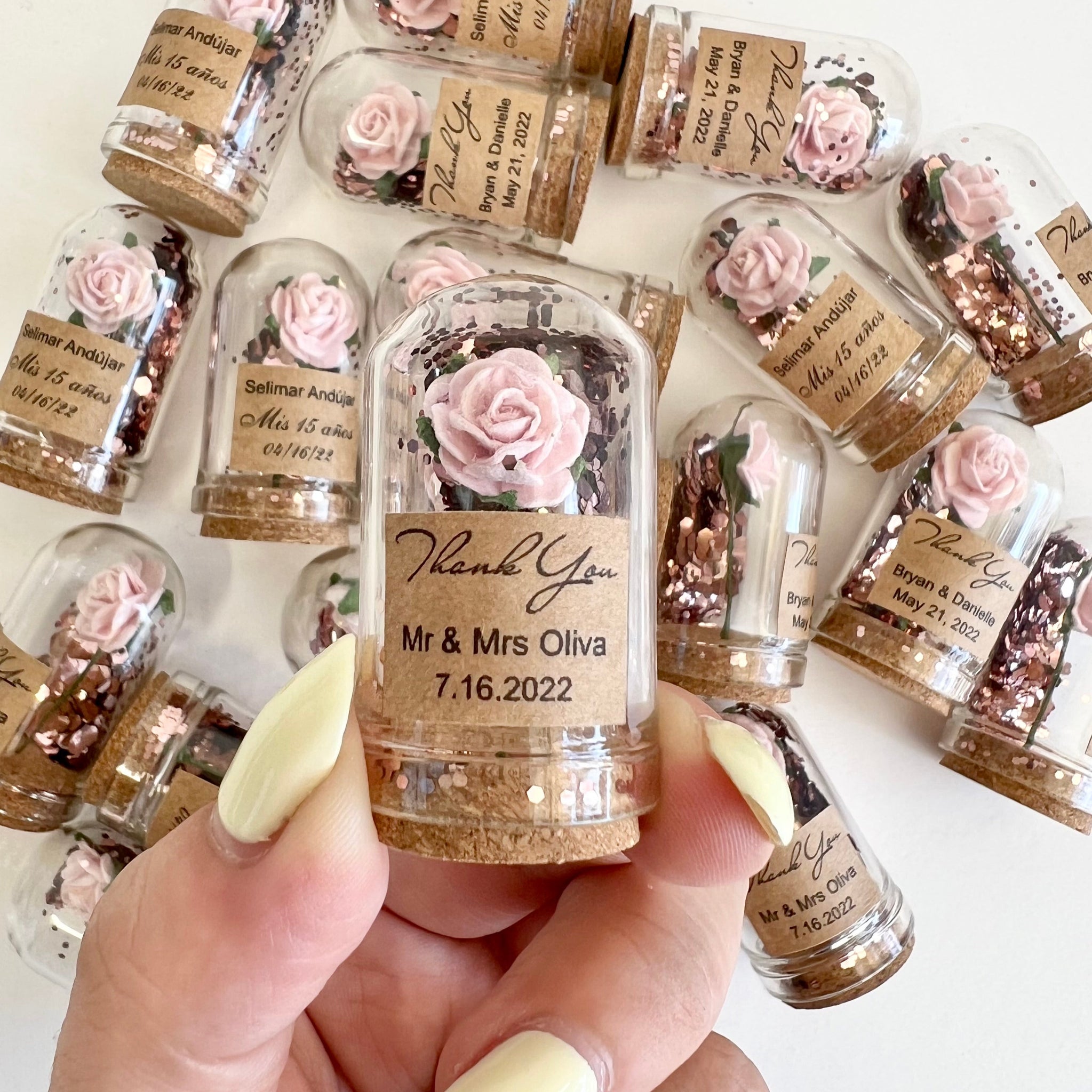 Personalized mini bottle favors with decorative labels held by a hand.