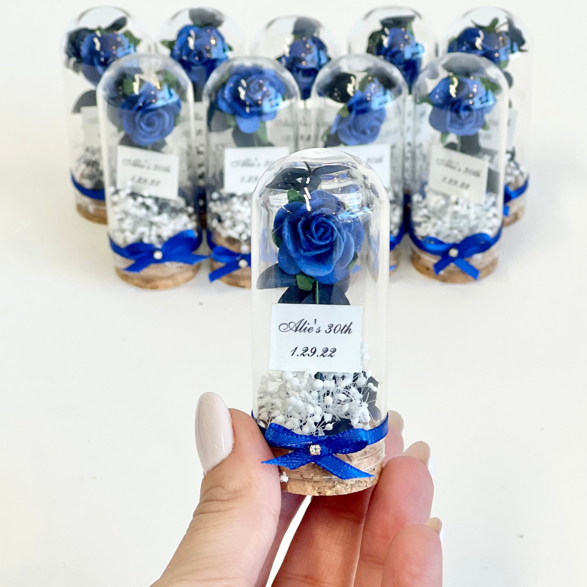 Decorative glass bottles with blue flowers and ribbons held by a hand on a white background