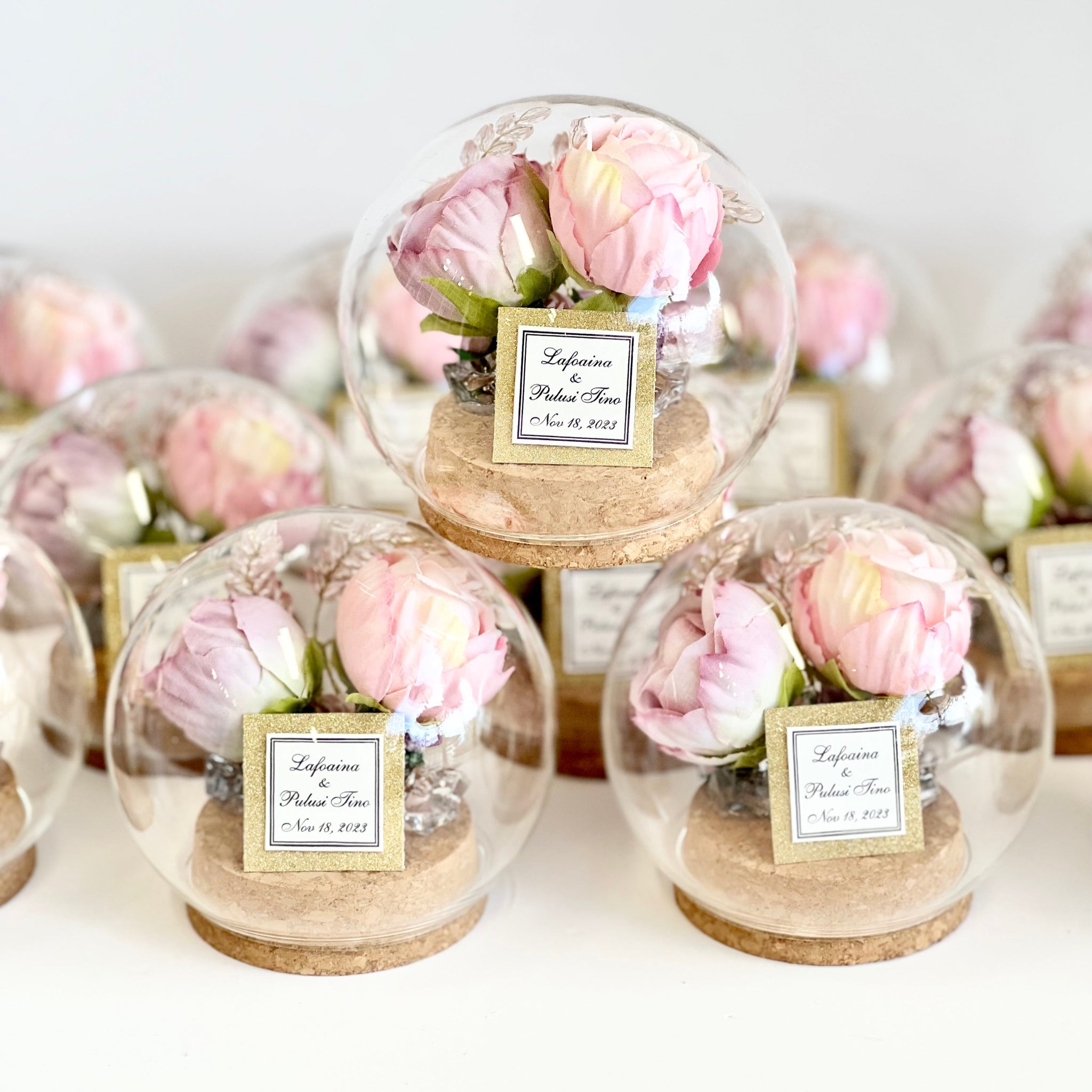 Decorative glass domes with pink flowers and name tags on a white background