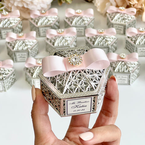 Decorative gift box with pink ribbon held by a hand, surrounded by similar boxes and flowers.