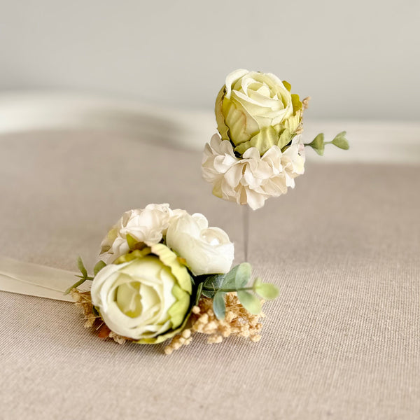 Two floral hair pins with white and green flowers on a neutral background