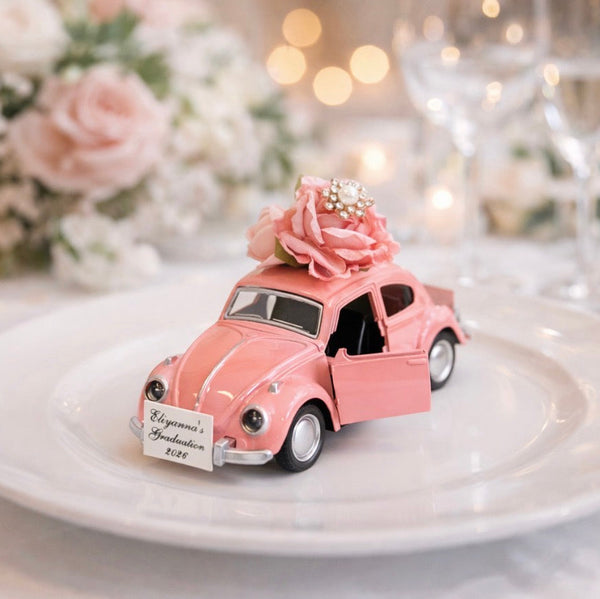 Pink toy car with flowers on a white plate, set against a blurred background of candles and flowers.