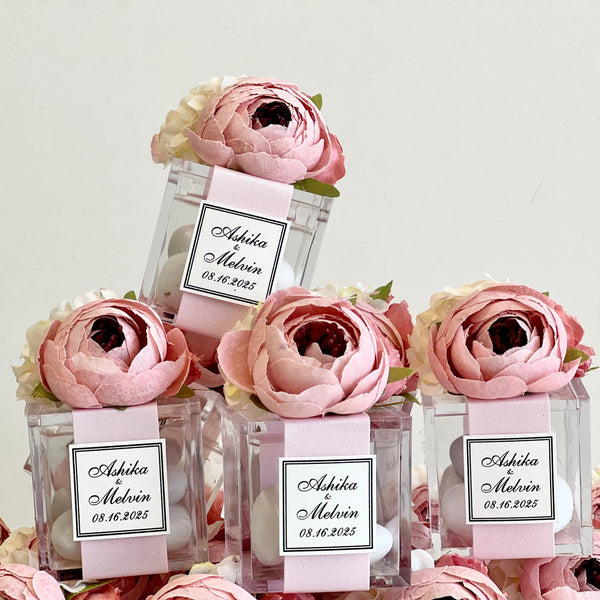 Small glass bottles with pink flowers and personalized labels on a light gray background