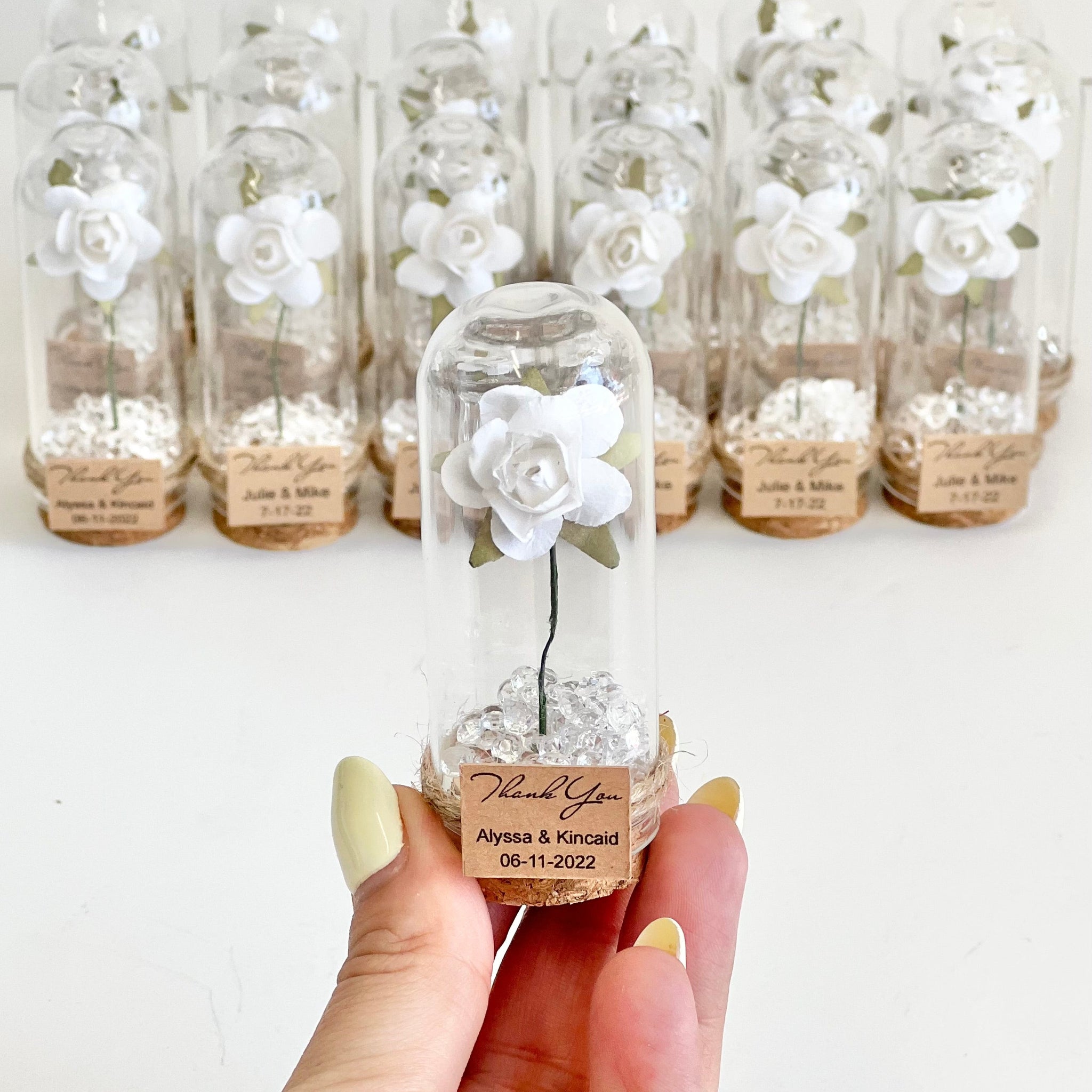 Clear glass bottle with decorative flower inside, held by a hand against a white background.