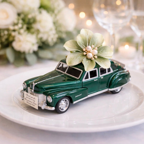 Green car-shaped favor on a white plate with flowers, surrounded by candles and flowers.