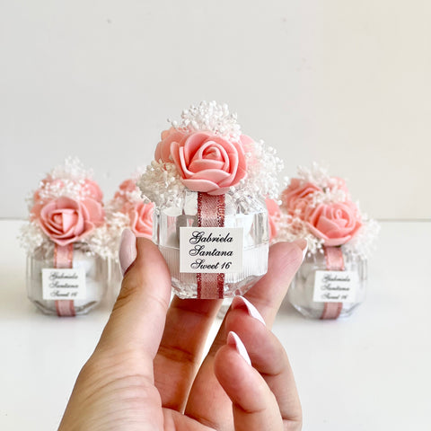 Small decorative bottle with pink roses and a white label held by a hand on a light background
