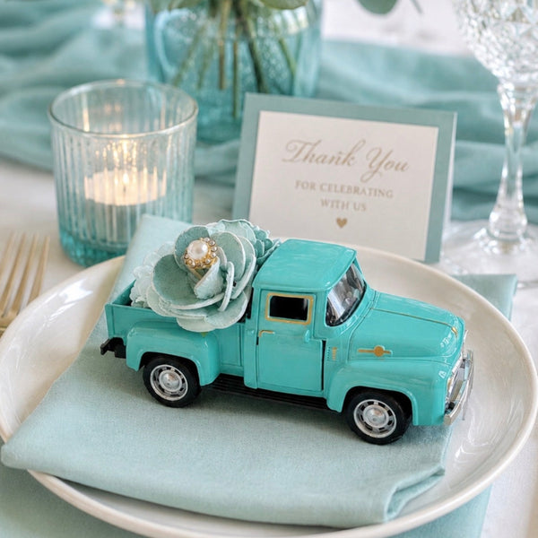 Teal toy truck on a plate with a card and flowers in the background