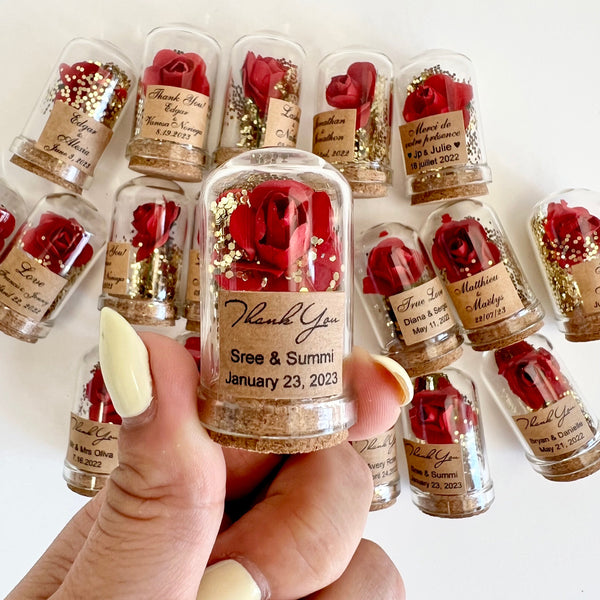 Small glass bottles with red roses and personalized labels held by a hand.