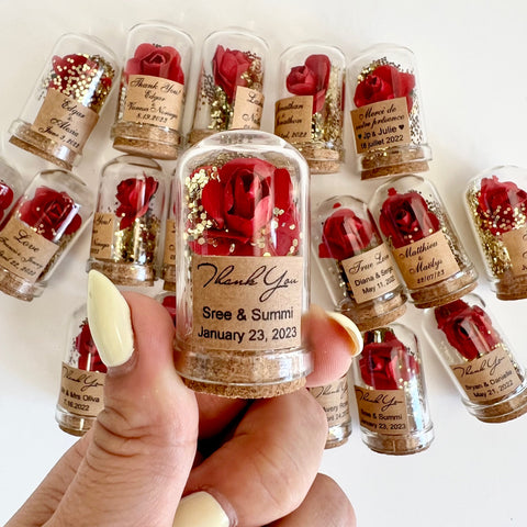 Small glass bottles with red roses and personalized labels held by a hand.