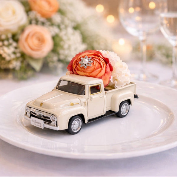 Model truck with flowers on a plate, set against a festive background with candles and flowers.