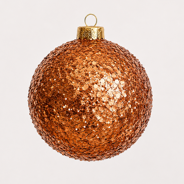 A round, coppery-rose gold Christmas ornament covered in dense glitter, featuring a gold cap and hanging loop, set against a plain light gray background.