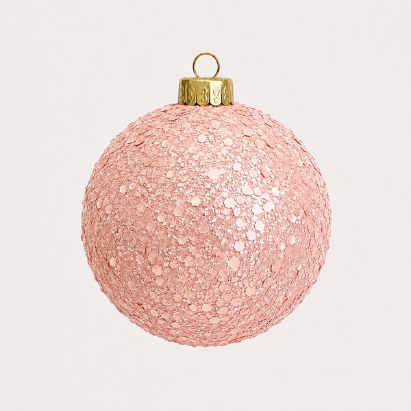 A spherical pink glitter Christmas ornament with a gold hanging cap and loop, shown against a plain light beige background.