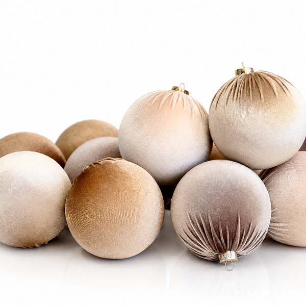A group of velvet Christmas ornaments in neutral shades of beige, cream, taupe, and light brown, arranged on a clean white background.