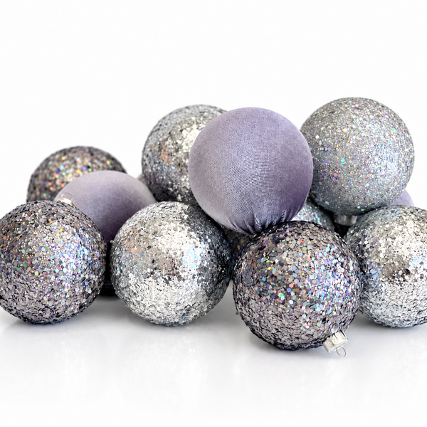 A group of decorative Christmas ornaments shaped like balls, featuring a mix of matte lavender velvet, silver glitter, and iridescent silver glitter finishes, arranged on a clean white background.