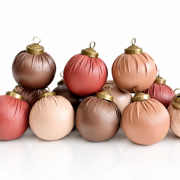 A group of ribbed Christmas ornament balls in assorted warm tones including brown, red, blush pink, and peach, each with a gold cap and loop, arranged on a white reflective surface.
