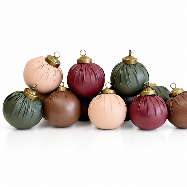 A group of matte fabric Christmas ornaments in muted earthy tones including sage green, dusty rose, burgundy, tan, and peach, each with a gold-tone metal cap and loop, arranged on a white background.
