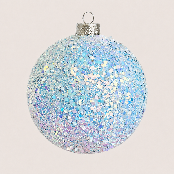 A spherical Christmas ornament covered in iridescent light blue and silver glitter, with a textured silver cap and hanging loop, shown against a plain light beige background.