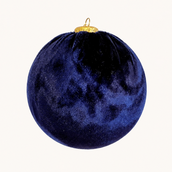 A spherical velvet Christmas ornament in deep navy blue with a small gold hanging loop at the top, shown against a plain off-white background.