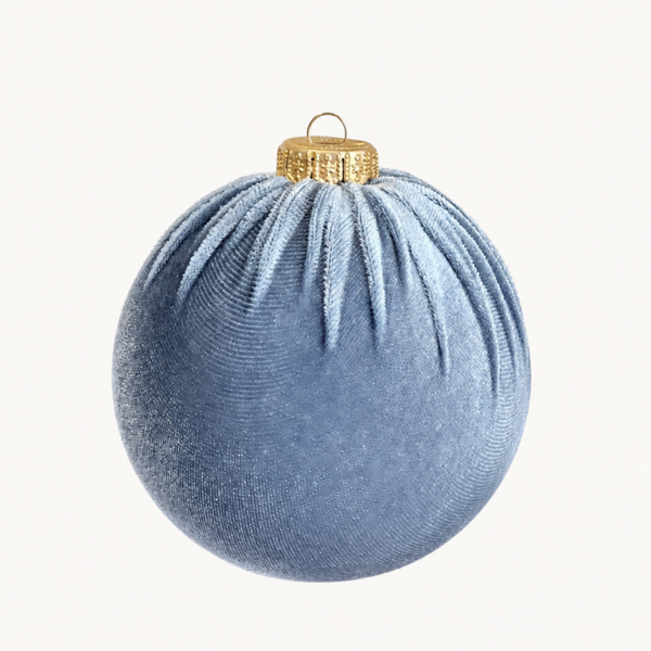 A light blue velvet Christmas ornament with a textured fabric surface and a gold metallic cap with a hanging loop, shown against a plain off-white background.