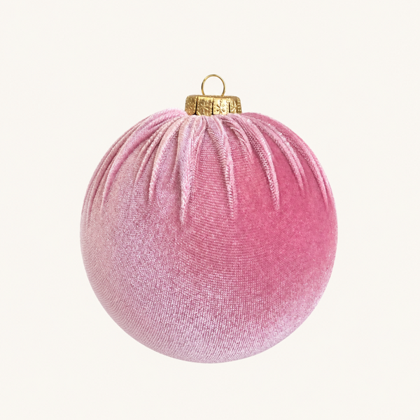 A pink velvet Christmas ornament with a gold metal cap and loop, shown against a plain off-white background.