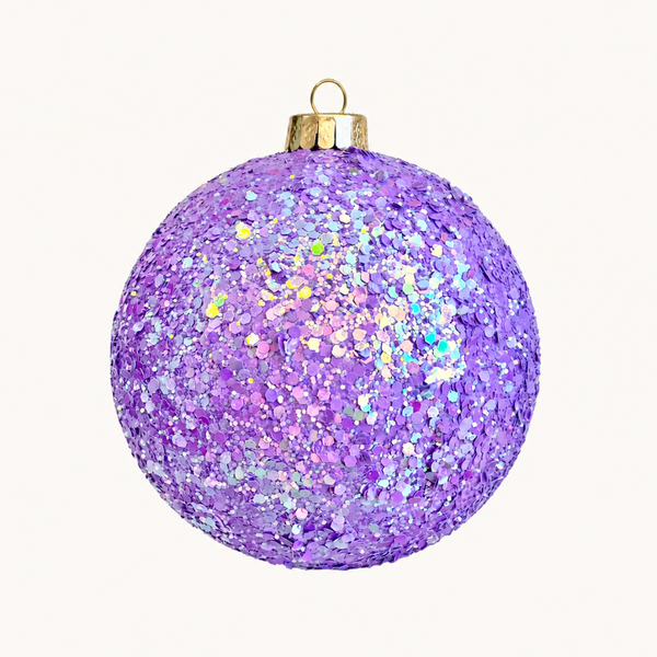 A spherical Christmas ornament covered in iridescent purple glitter, featuring a gold metal cap and hanging loop, set against a solid off-white background.