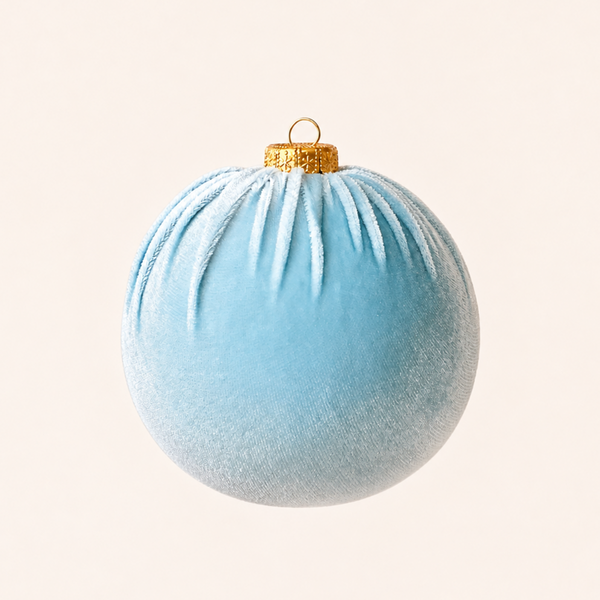 A light blue velvet Christmas ornament with a gold hanging loop and cap, centered against a solid cream background.