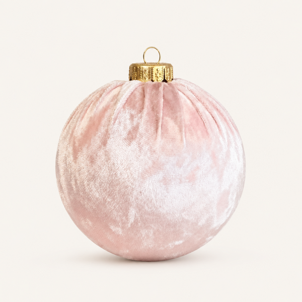 A round pink velvet Christmas ornament with a textured, velvety surface and a gold metal cap with a hanging loop, shown on a clean off-white background.