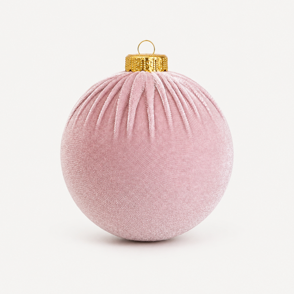 A dusty pink velvet Christmas ornament with a textured fabric surface, pleated details, and a gold metallic cap with a hanging loop, shown on a clean off-white background.