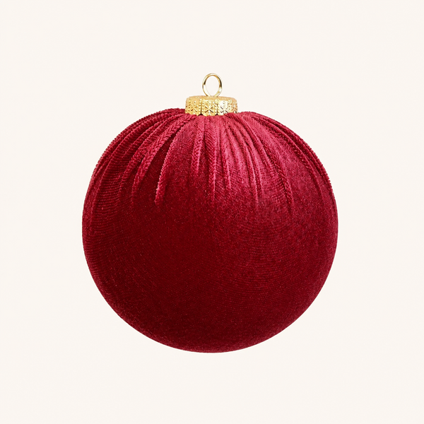 A deep red velvet Christmas ornament with a gold hanging loop and cap, centered on a light cream background.