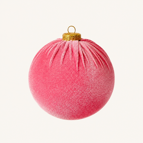A round pink velvet Christmas ornament with a gold metallic cap and hanging loop, centered on a light cream background.