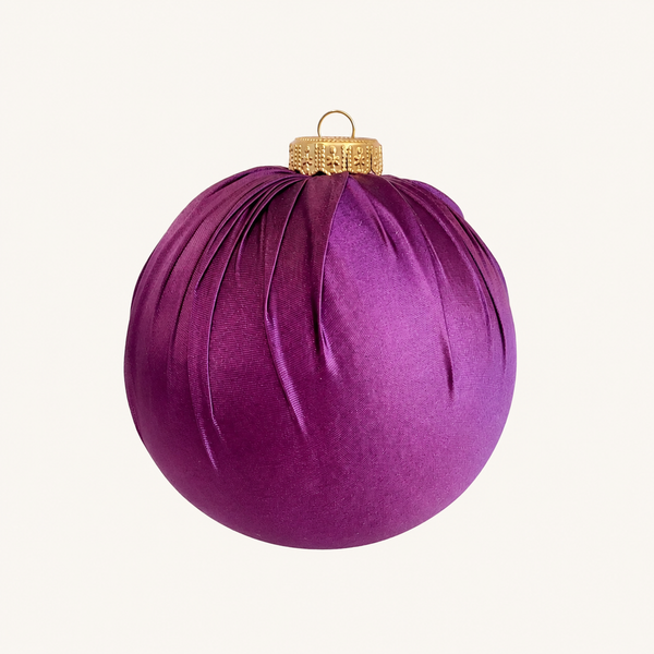 A purple velvet Christmas ornament with a gold metal cap and hanging loop, shown against a plain off-white background.