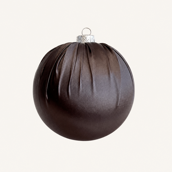 A dark brown pleated fabric Christmas ornament with a silver hanging loop, shown against a solid off-white background.