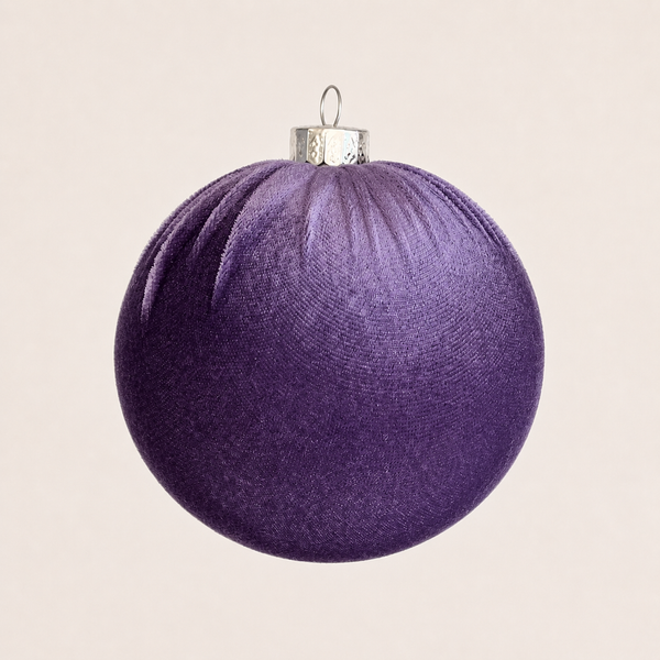 A textured purple Christmas ornament ball with a silver metal cap and loop, shown against a solid light beige background.