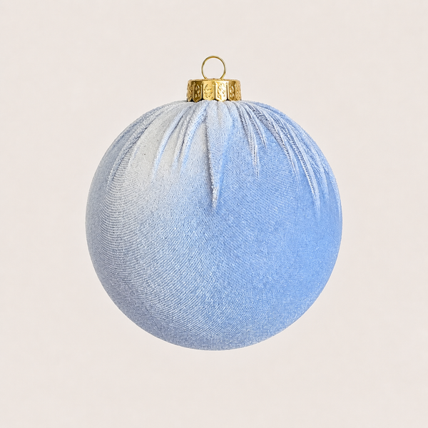 A light blue textured fabric Christmas ornament with a gold metal cap and hanging loop, shown against a solid light beige background.
