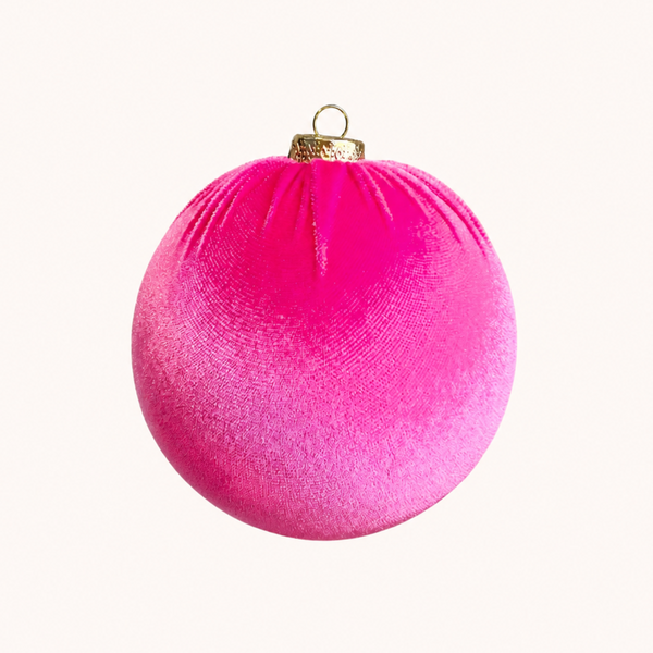 A bright pink velvet Christmas ornament with a gold metal cap and hanging loop, centered on a solid off-white background.