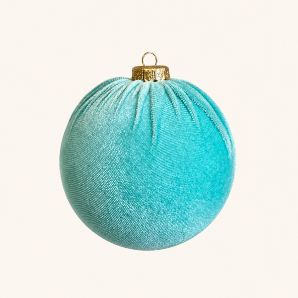 A round, textured teal velvet Christmas ornament with a gold cap and hanging loop, centered on a solid off-white background.
