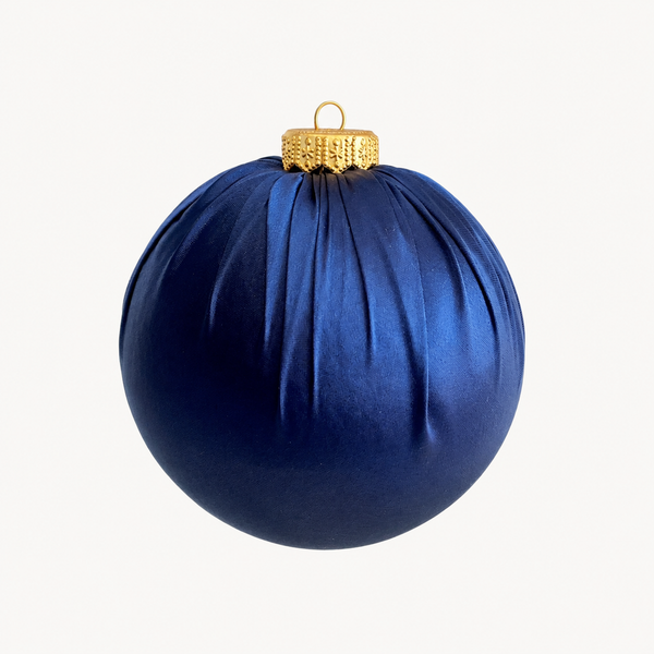 A dark blue pleated fabric Christmas ornament with a textured gold cap and hanging loop, shown against a plain off-white background.