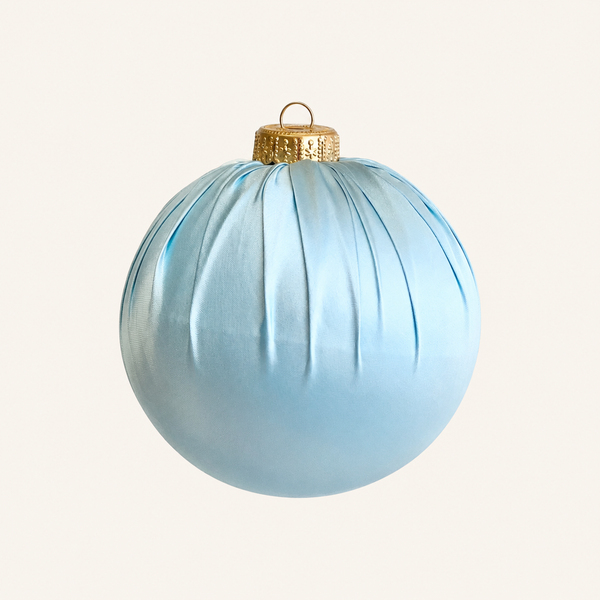 A light blue ribbed Christmas ornament with a textured gold cap and hanging loop, shown against a solid off-white background.