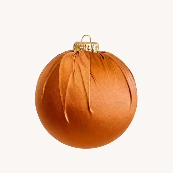 A single warm copper-orange Christmas ornament with a textured fabric-like surface, a gold cap, and a hanging loop, centered on a plain light background.
