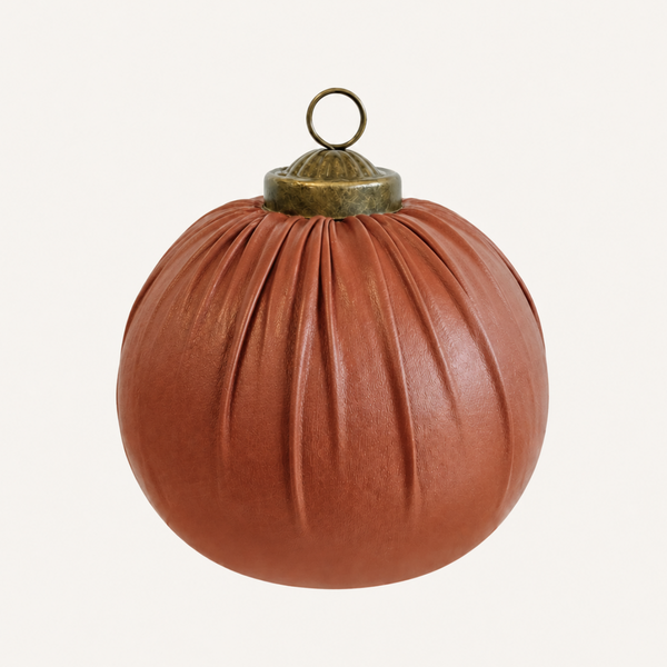 A terracotta-colored leather Christmas ornament shaped like a pleated pumpkin, featuring a brass hanging loop at the top, set against a plain off-white background.