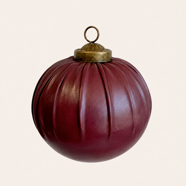 A ribbed, glossy dark red leather ornament shaped like a pumpkin, featuring a brass hanging loop at the top, set against a solid off-white background.