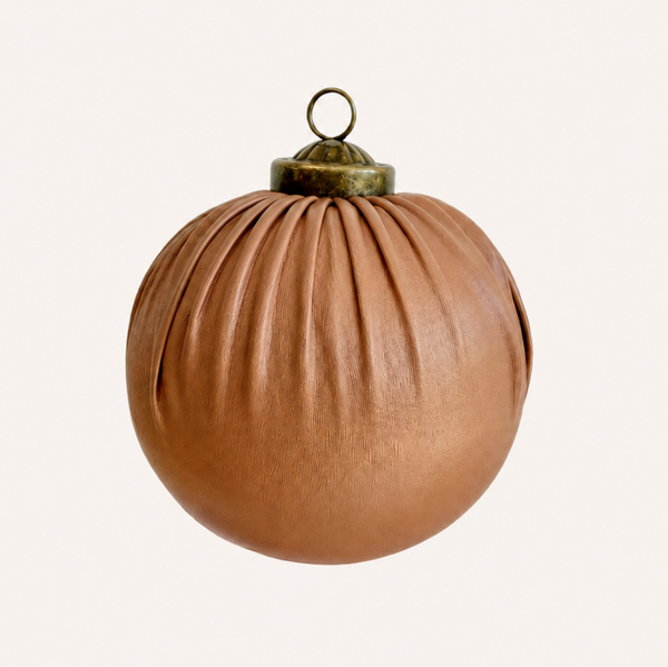 A spherical brown leather ornament with vertical pleats and a brass hanging loop at the top, shown against a plain off-white background.