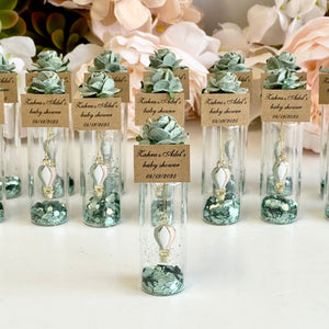 Decorative bottles with greenery and labels on a white surface with flowers in the background
