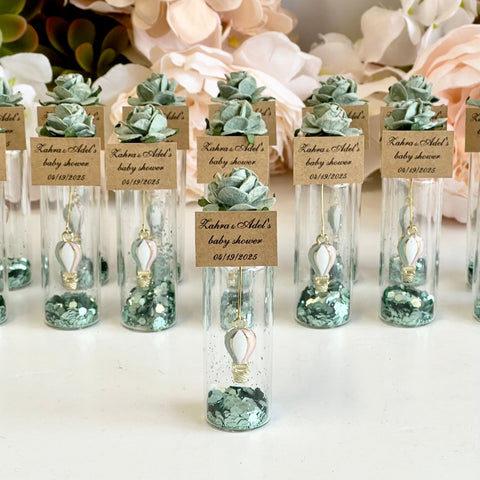 Decorative bottles with greenery and labels on a white surface with flowers in the background