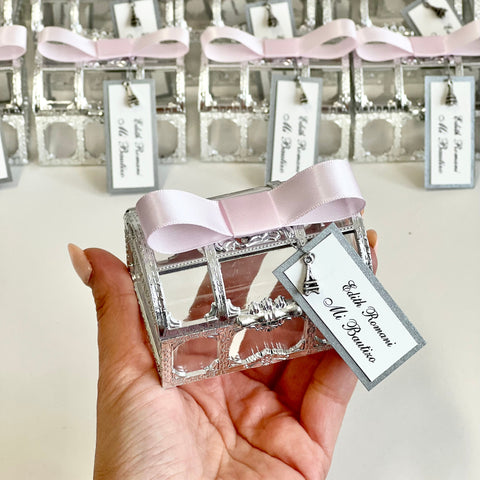 Silver decorative box with pink ribbon held by a hand, with more boxes in the background.