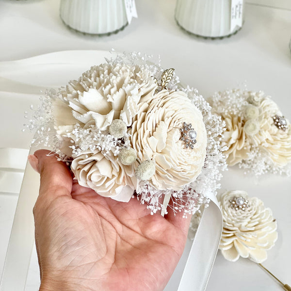 Hand holding a decorative flower arrangement with white flowers and ribbons on a light background